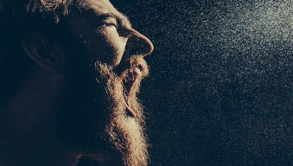Naked bearded man angrily screams into a spray of water against a black background with copy space