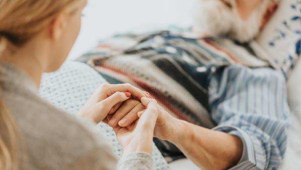 Młoda kobieta trzyma w dłoniach rękę swojego umierającego w szpitalu ojca