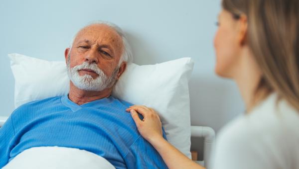 Sick man looking at upset daughter while lying on bed in hospital