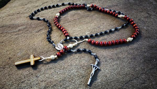 Two entwined rosaries, one black and one brownish red, placed on a slab of granite.