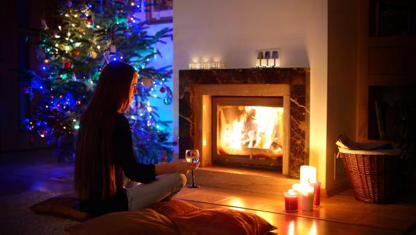Woman having a drink by a fireplace in a cozy dark living room on Christmas eve