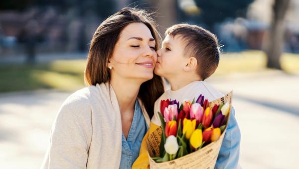 A little boy giving bouquet of tulips to his mother and kissing her on mother's day