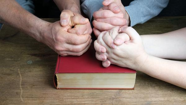 Dłonie ludzi złożone na Biblii