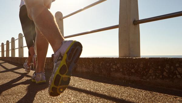 Pareja, piernas y correr con sol en el paseo marítimo para hacer ejercicio, ejercicio cardiovascular o entrenamiento al aire libre. Personas activas, o corredores con zapatos o zapatillas de deporte para la actividad física, la salud o el bienestar