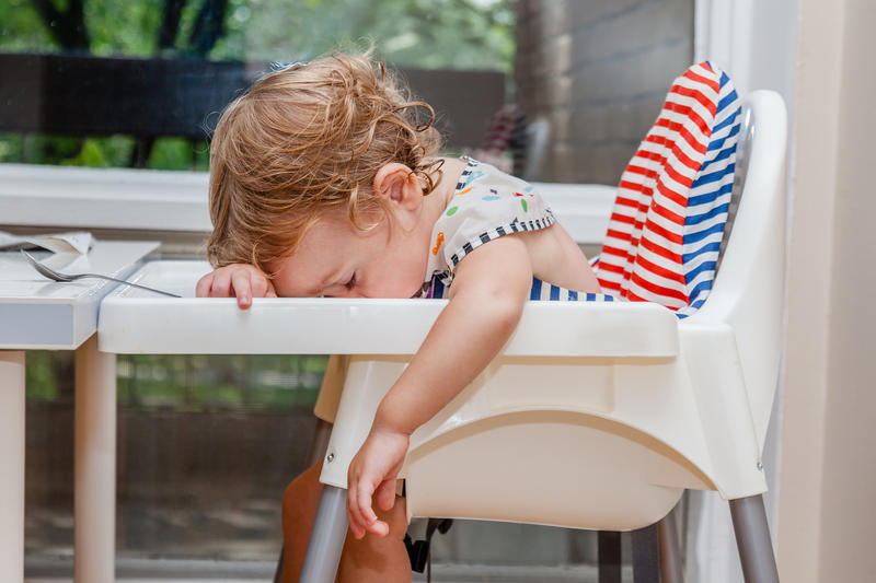 Tired child sleeping in highchair after the lunch. Baby over eating and fall asleep just after feeding, lying his face on the table tray.