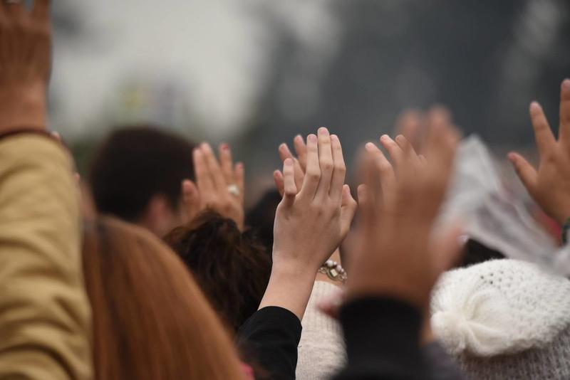 PESSOAS NA MISSA COM MÃOS ERGUIDAS