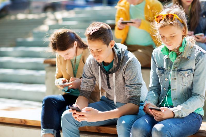 grupa nastolatków siedzi na schodach i wpatruje się w smartfony